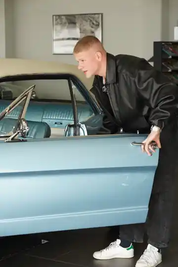 Luis Kummer an einem hellblauen Oldtimer in einem modernen Innenraum