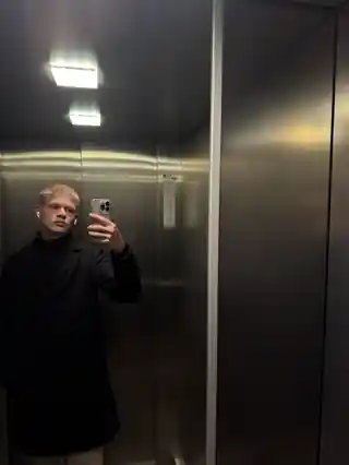 Luis Kummer bei einem Spiegelselfie im Aufzug in dunklem Mantel